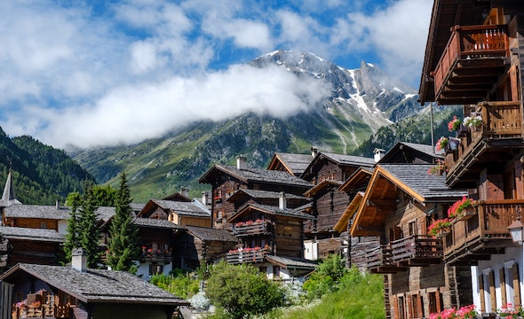 Wooden homes on a steep lush hill beneath a tall mountain